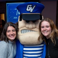 Girl in grey dress and girl in black shirt pose with Louie the Laker